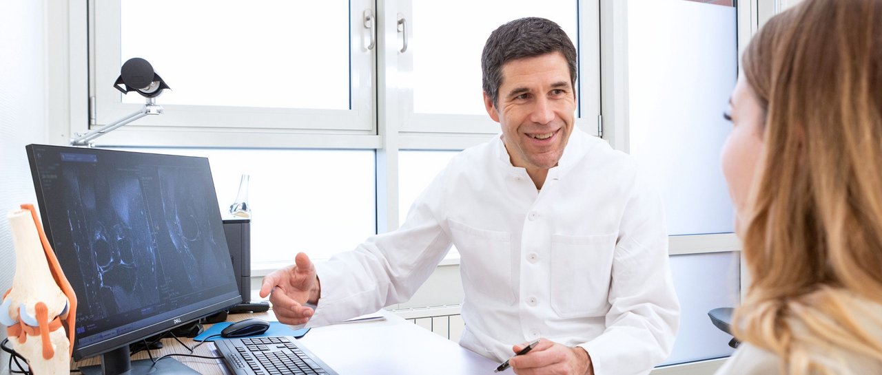 Ein Arzt zeigt einer Patientin ein Röntgenbild an seinem PC