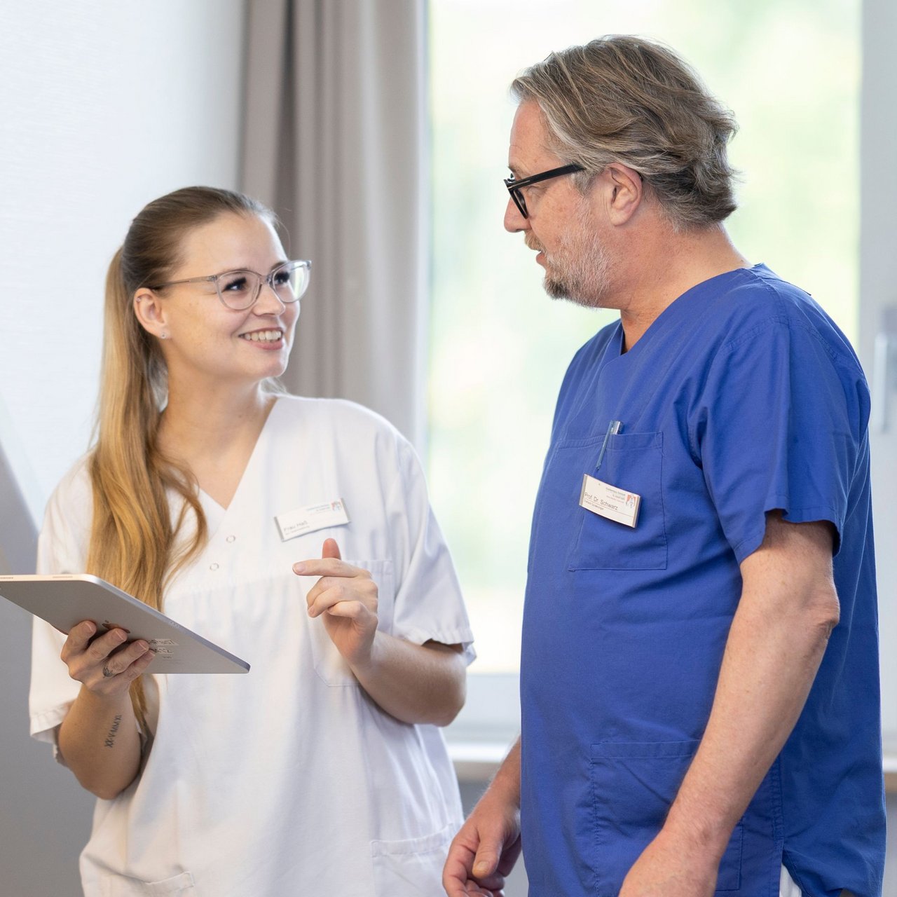 Eine Pflegerin hält ein Tablet und bespricht etwas mit einem Arzt am Patientenbett