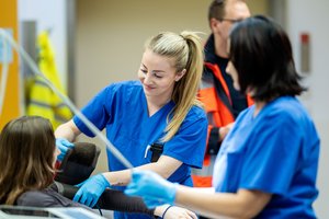 Eine Pflegerin in der Notaufnahme misst den Puls einer Patientin, ihre Kollegin hilft dabei