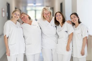 5 Pflegerinnen auf den Flur umarmen sich und lachen in die Kamera