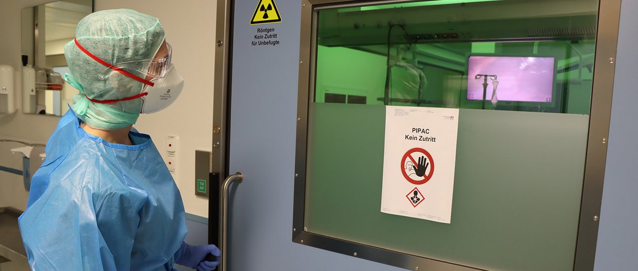 Der Chirurg steht mit Schutzkleidung vor dem OP-Saal, in dem eine Vernebelung stattfindet - Nicht Betreten-Schild an OP-Tür. 