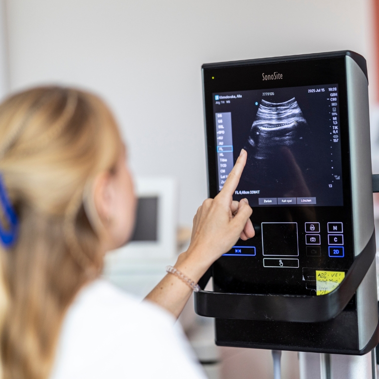Eine Frau zeigt auf einen Ultraschallmonitor, auf dem das ungeborene Baby zu sehen ist.
