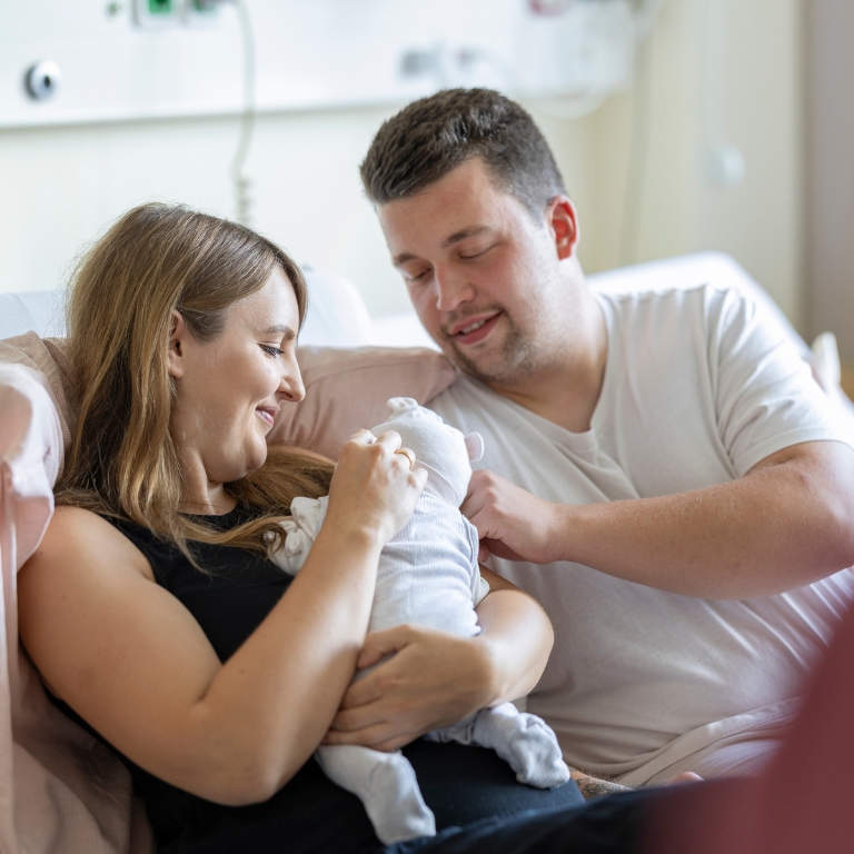 Mutter und Vater sitzen zusammen und halten ihr neugeborenes Baby im Arm.
