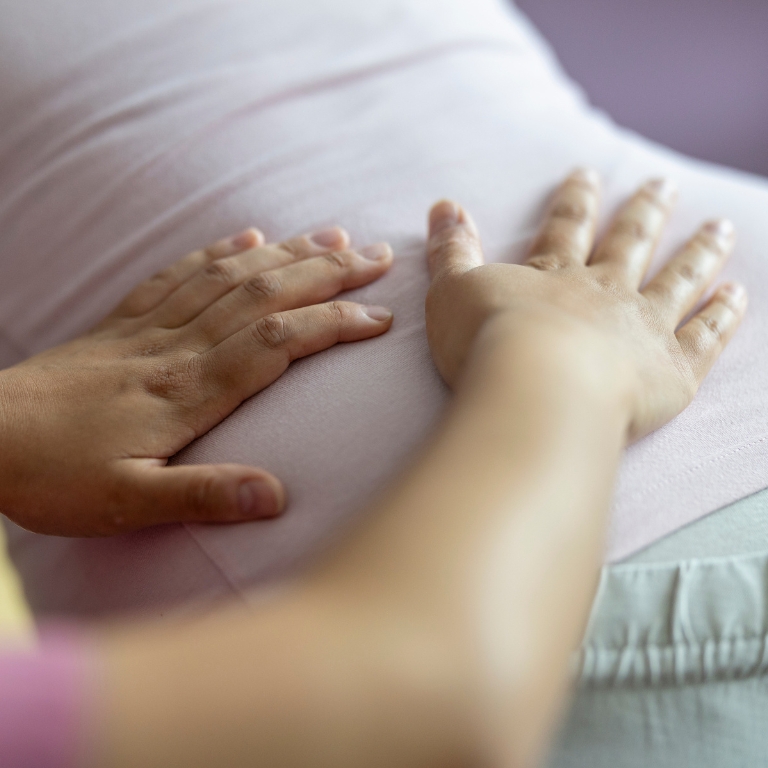 Zwei Hände liegen auf dem Bauch einer schwangeren Frau und berühren ihn sanft.