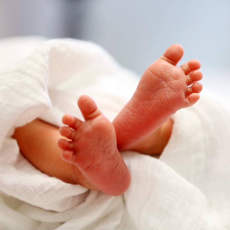 Kleine Babyfüße liegen auf einer weichen Decke.