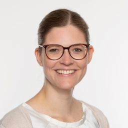 Lächelnde Frau mit Brille vor neutralem Hintergrund.