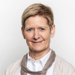 Porträt einer Frau mit kurzem Haar vor neutralem Hintergrund.