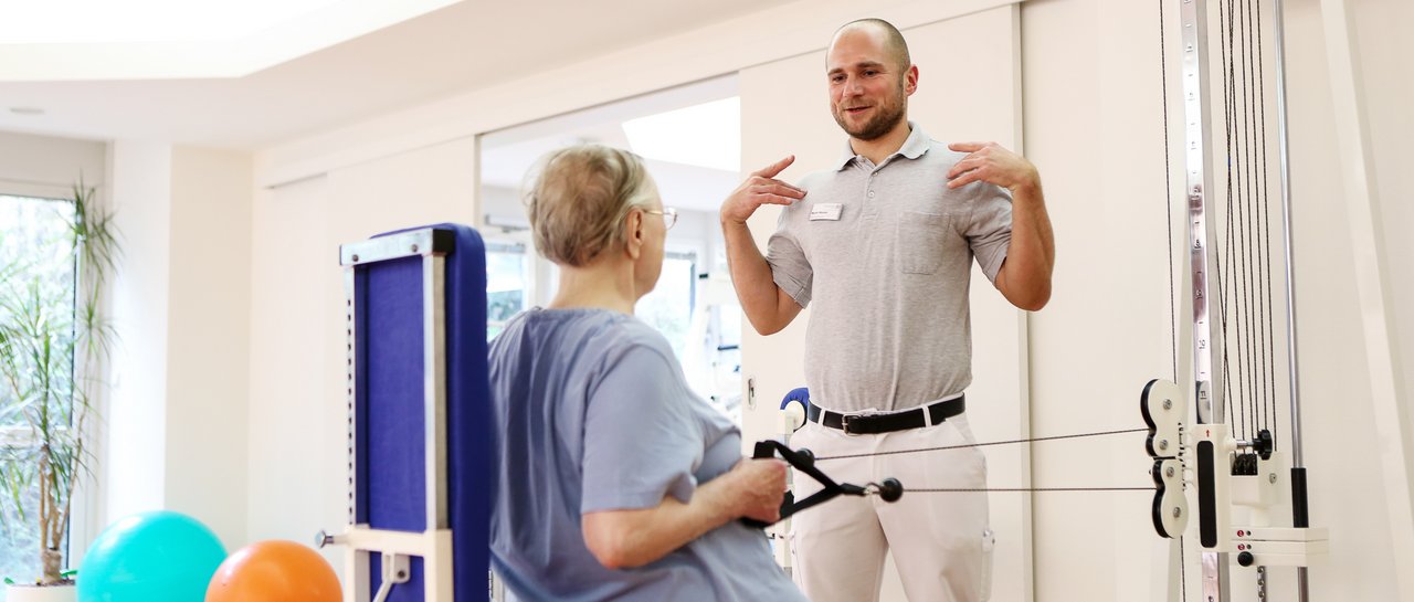 Ein Physiotherapeut zeigt einer Patientin eine Übung für die Schultern