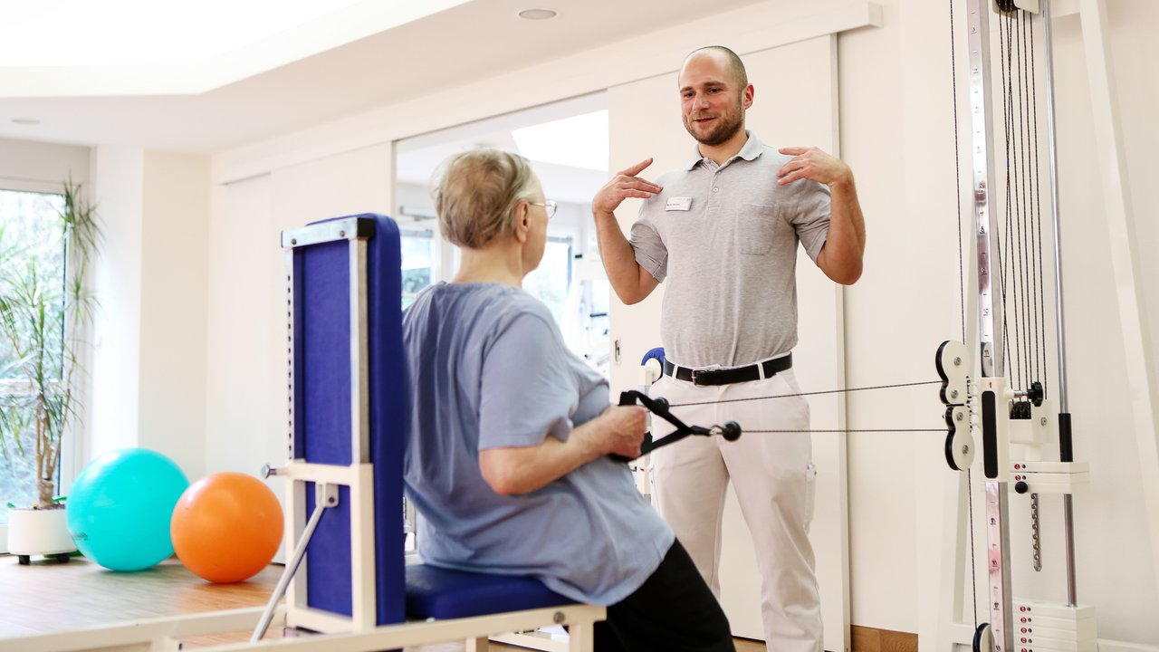 Ein Physiotherapeut zeigt einer Patientin eine Übung für die Schultern