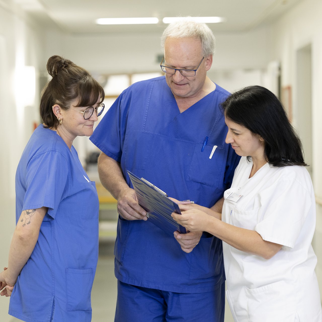 Ein Oberarzt und 2 Pflegerinnen stehen auf dem Flur der Kardiologie und besprechen einen Fall am Tablet.
