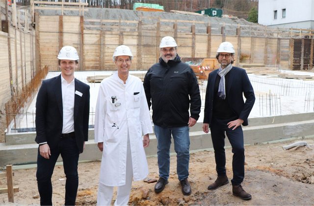 Vier Männer mit Bauhelmen stehen auf einer Baustelle am Krankenhaus Reinbek vor einem im Bau befindlichen Fundament.