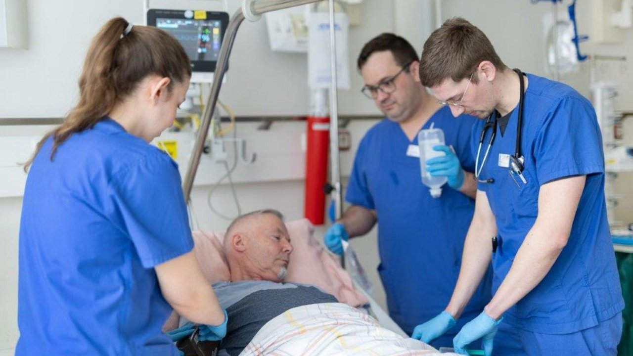 Ein Neurologiepatient wird von 3 Pflegekräften am Krankenhausbett versorgt