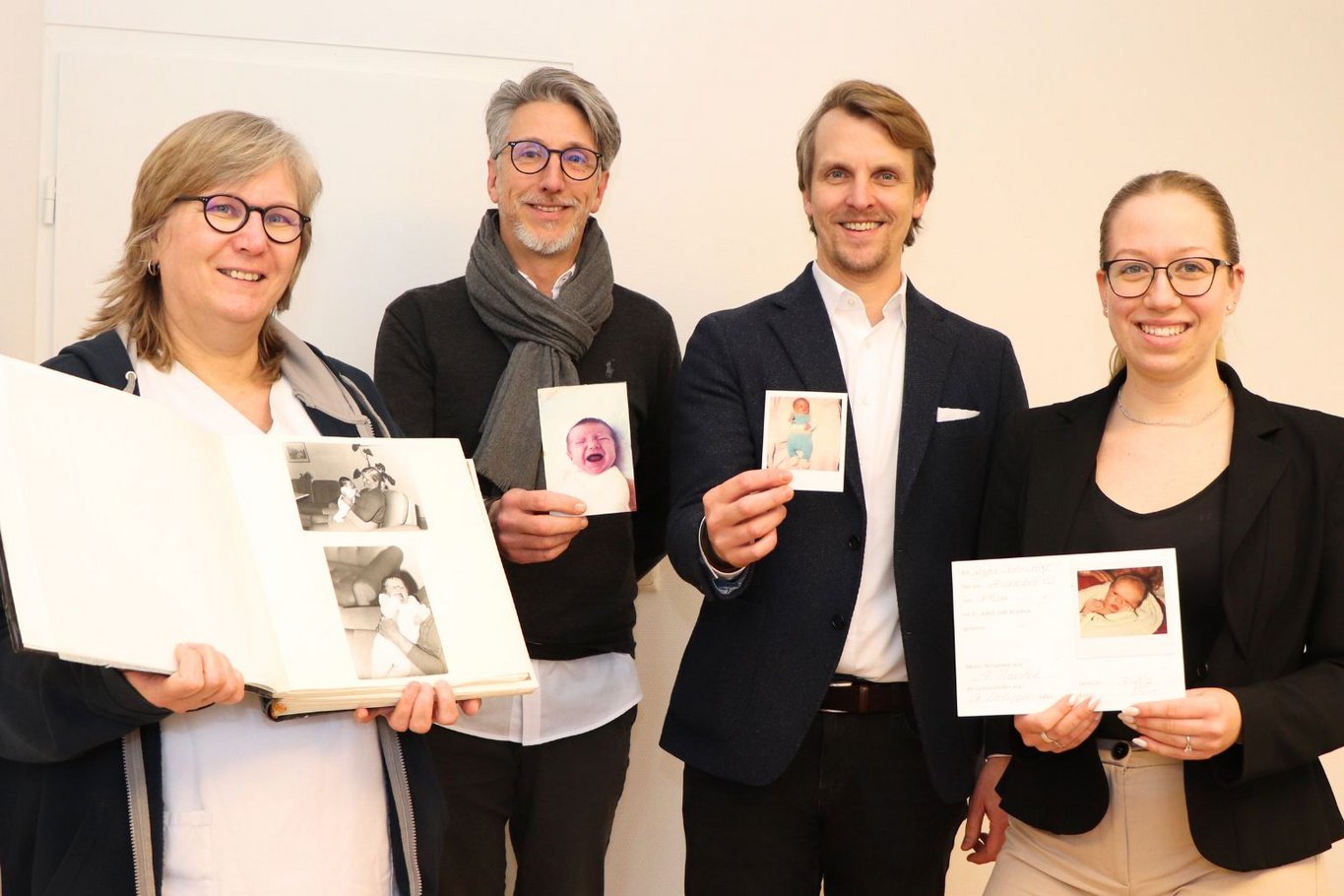 Vier Mitarbeitende des St. Adolf-Stifts stehen nebeneinander und halten persönliche Babyfotos sowie ein Fotoalbum aus unterschiedlichen Jahrzehnten in die Kamera.