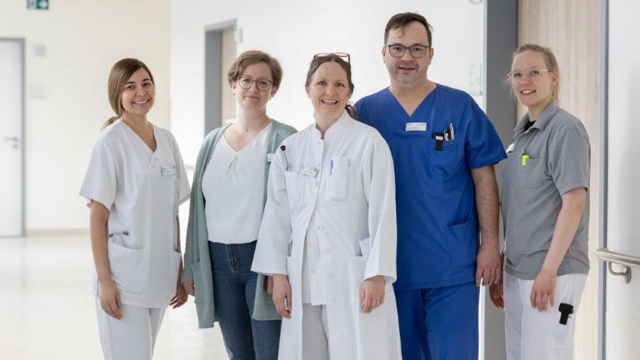 Das Team der Neurologie steht auf dem Krankenhausflur und lächelt in die Kamera