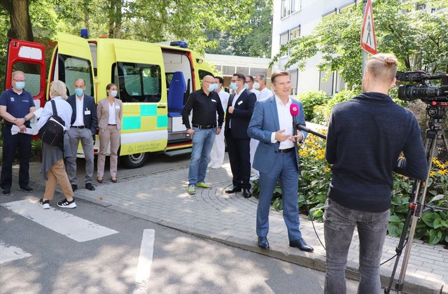 Mann gibt vor einem Rettungswagen ein Interview vor laufender Kamera.