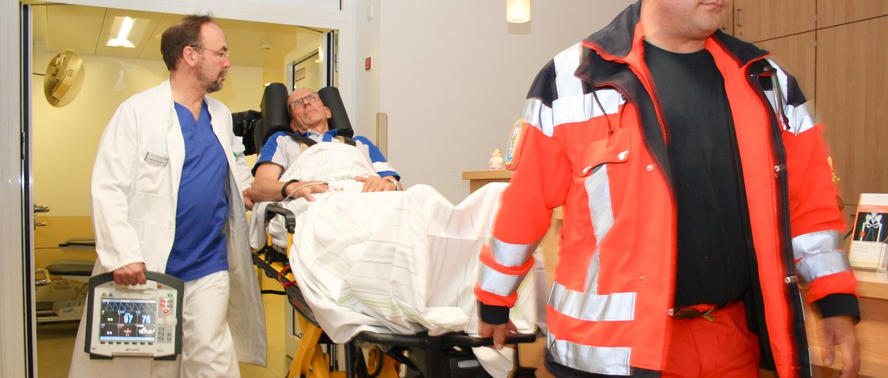 Ein Mann auf einer Krankenliege wird von einem Rettungssanitäter und einem Notarzt in die Notaufnahme gefahren