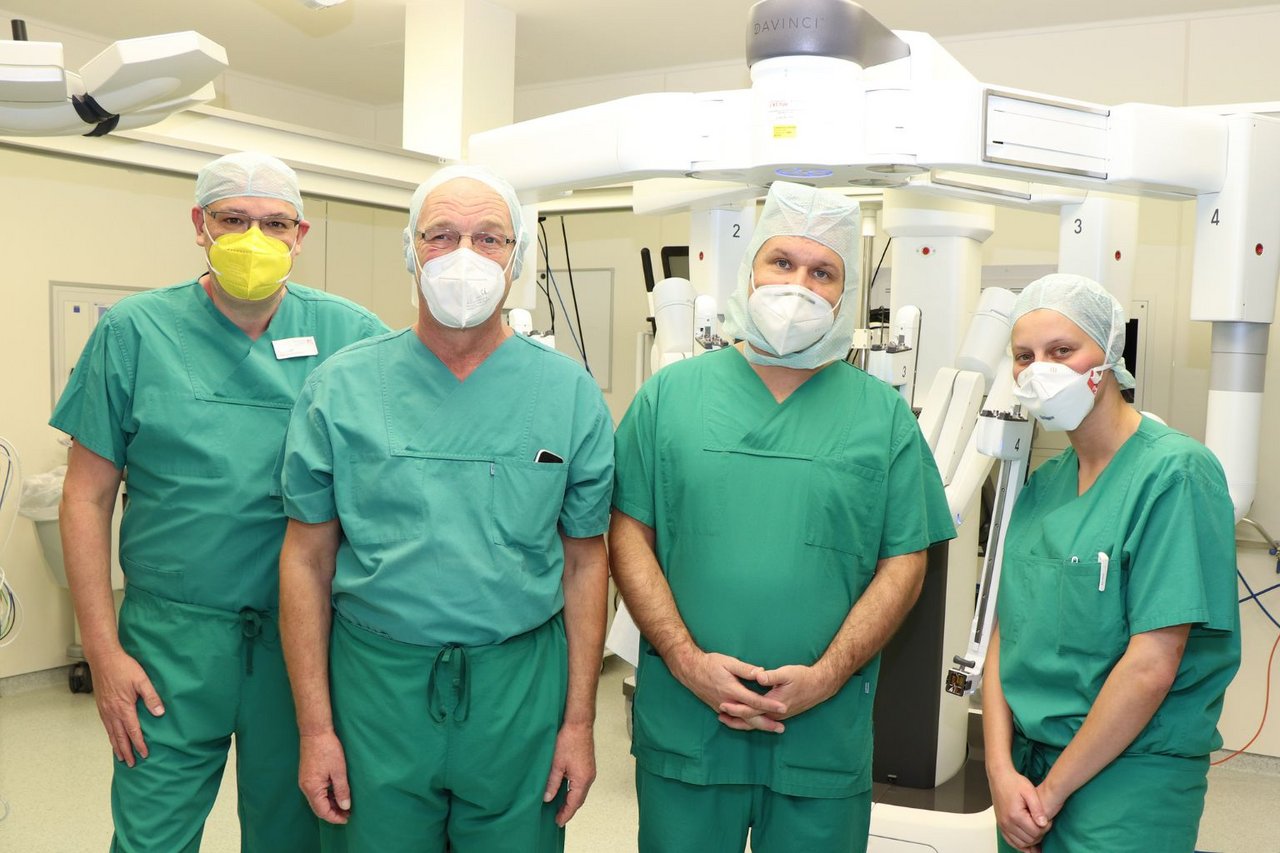 Vier Mitglieder des OP-Teams in Schutzkleidung stehen vor einem da Vinci-Operationssystem und blicken in die Kamera.
