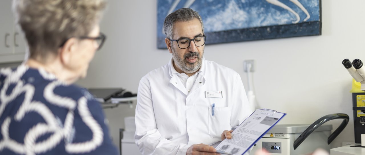 Ein Oberarzt zeigt einer älteren Patientin etwas auf einem Klemmbrett