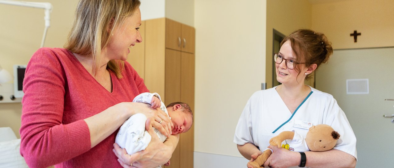 Eine Mutter hält ihr Baby im Arm und eine Pflegerin spricht mit ihr