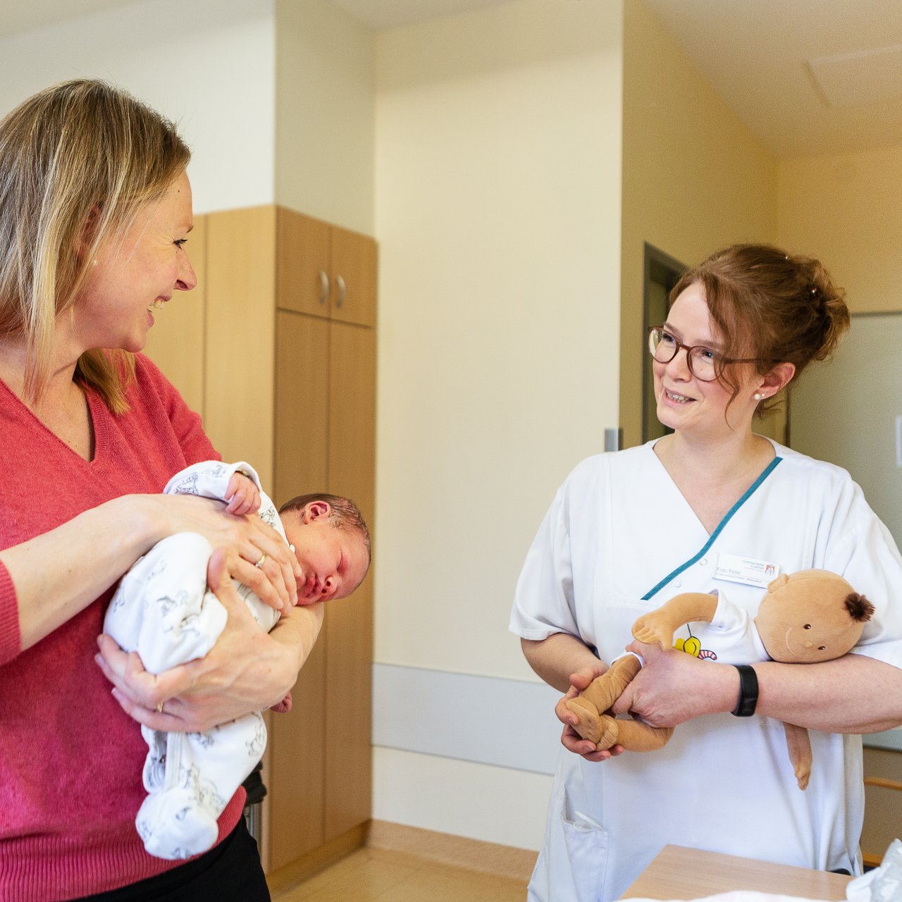 Eine Mutter hält ihr Baby im Arm und eine Pflegerin spricht mit ihr