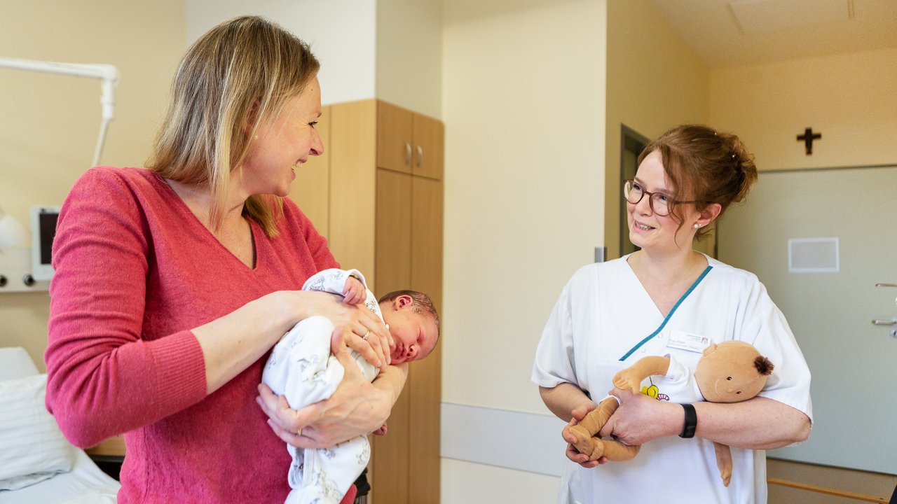 Eine Mutter hält ihr Baby im Arm und eine Pflegerin spricht mit ihr