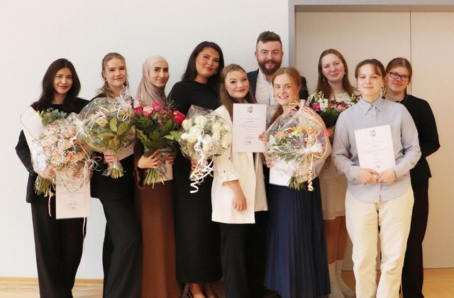 Zehn frisch examinierte Pflegekräfte stehen für ein Gruppenfoto zusammen und halten ihre Abschlussurkunden und Blumensträuße.