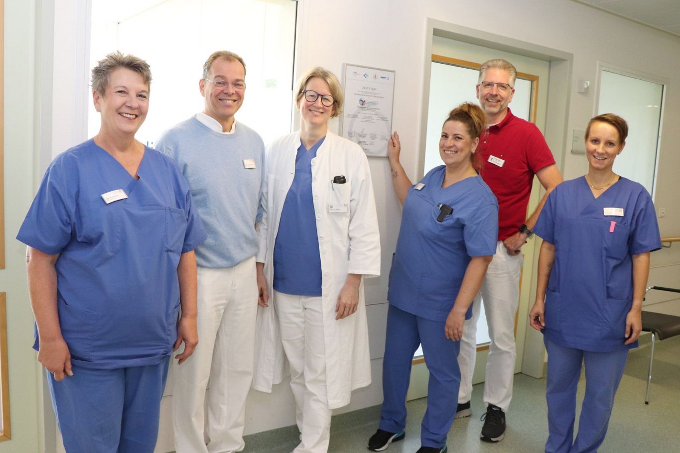 Sechs Mitarbeitende des Krankenhauses Reinbek stehen gemeinsam in einem Flur und lächeln in die Kamera, darunter medizinisches Fachpersonal und Ärzte in Arbeitskleidung.