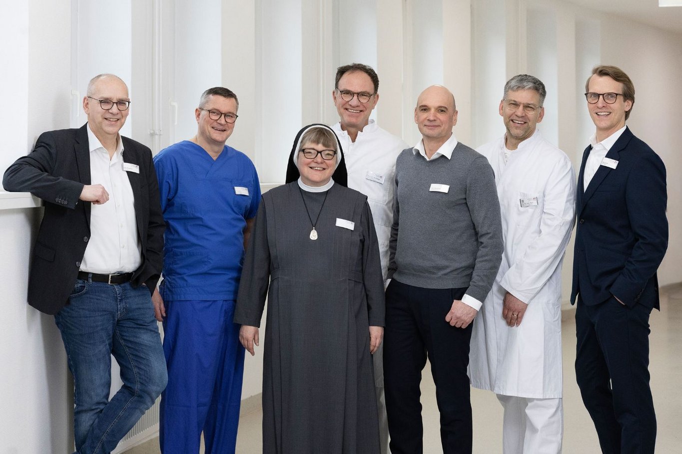 Sieben Personen stehen in einem Flur nebeneinander und lächeln. 