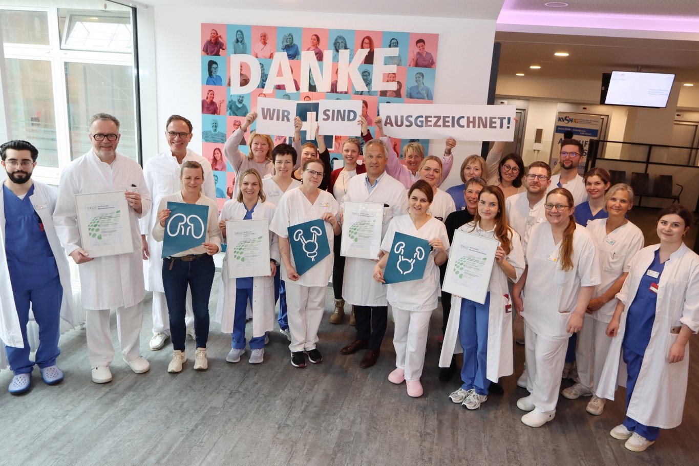 Großes Team aus medizinischem Personal im Krankenhaus Reinbek steht gemeinsam in einem Flur und hält Zertifikate sowie Schilder hoch, im Hintergrund ein Banner mit der Aufschrift „Danke – wir sind ausgezeichnet!“.