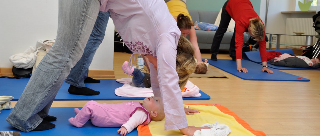 Eine Mama macht Yoga und schaut auf ihr Baby herab
