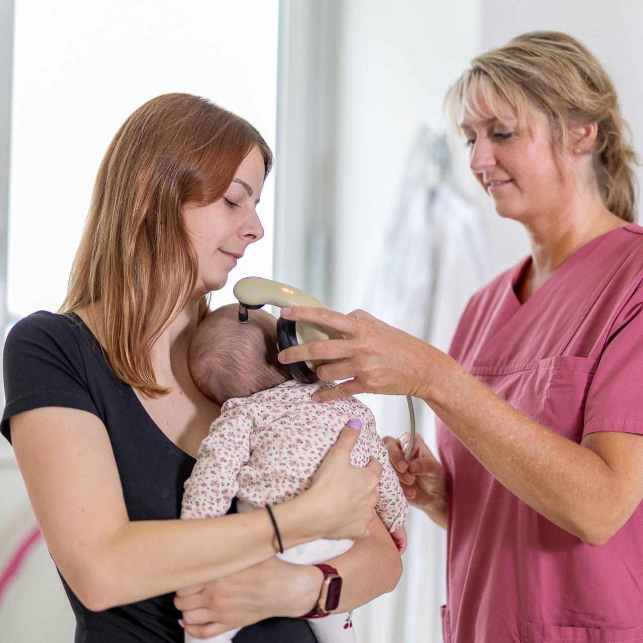 Eine Pflegerin führt einen Hörtest mit einem Baby durch, das von seiner Mutter gehalten wird