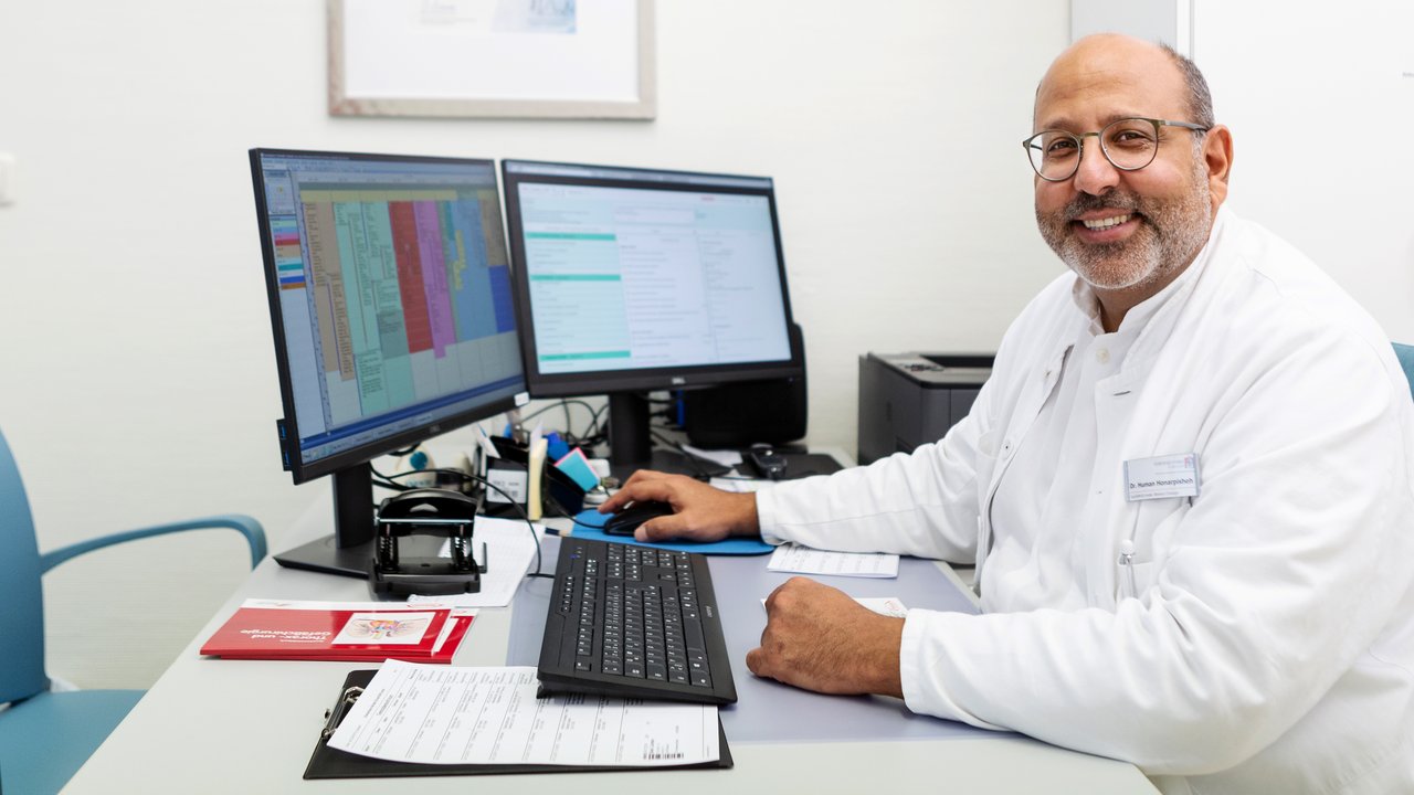 Ein Arzt sitzt am Computer und lächelt in die Kamera