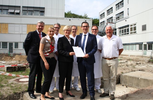 Mehrere Vertreter aus Politik und Krankenhaus stehen auf einer Baustelle am Krankenhaus Reinbek St. Adolf-Stift und präsentieren einen Förderbescheid für Bauprojekte.