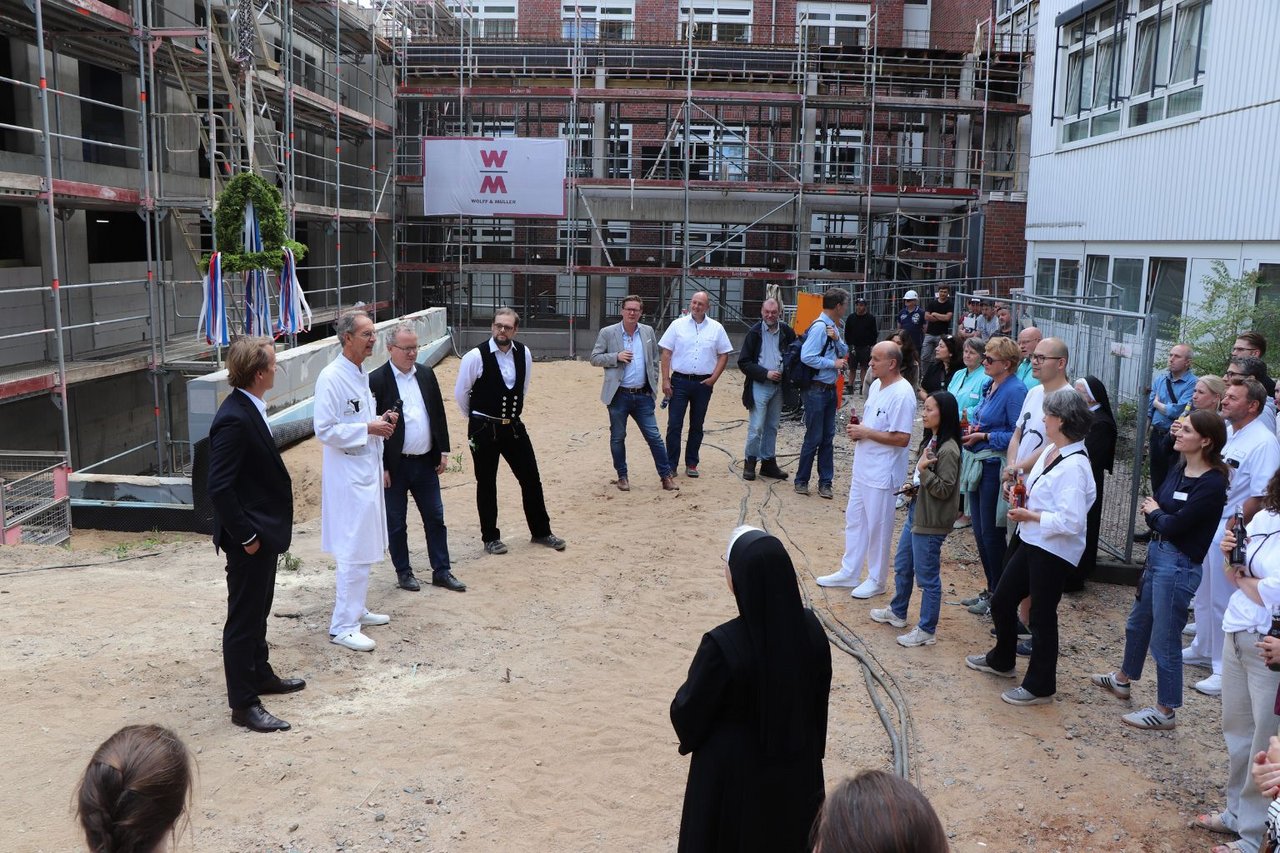 Mehrere Mitarbeitende und Gäste stehen auf der Baustelle des Neubaus am Krankenhaus Reinbek und hören einer Ansprache beim Richtfest zu.