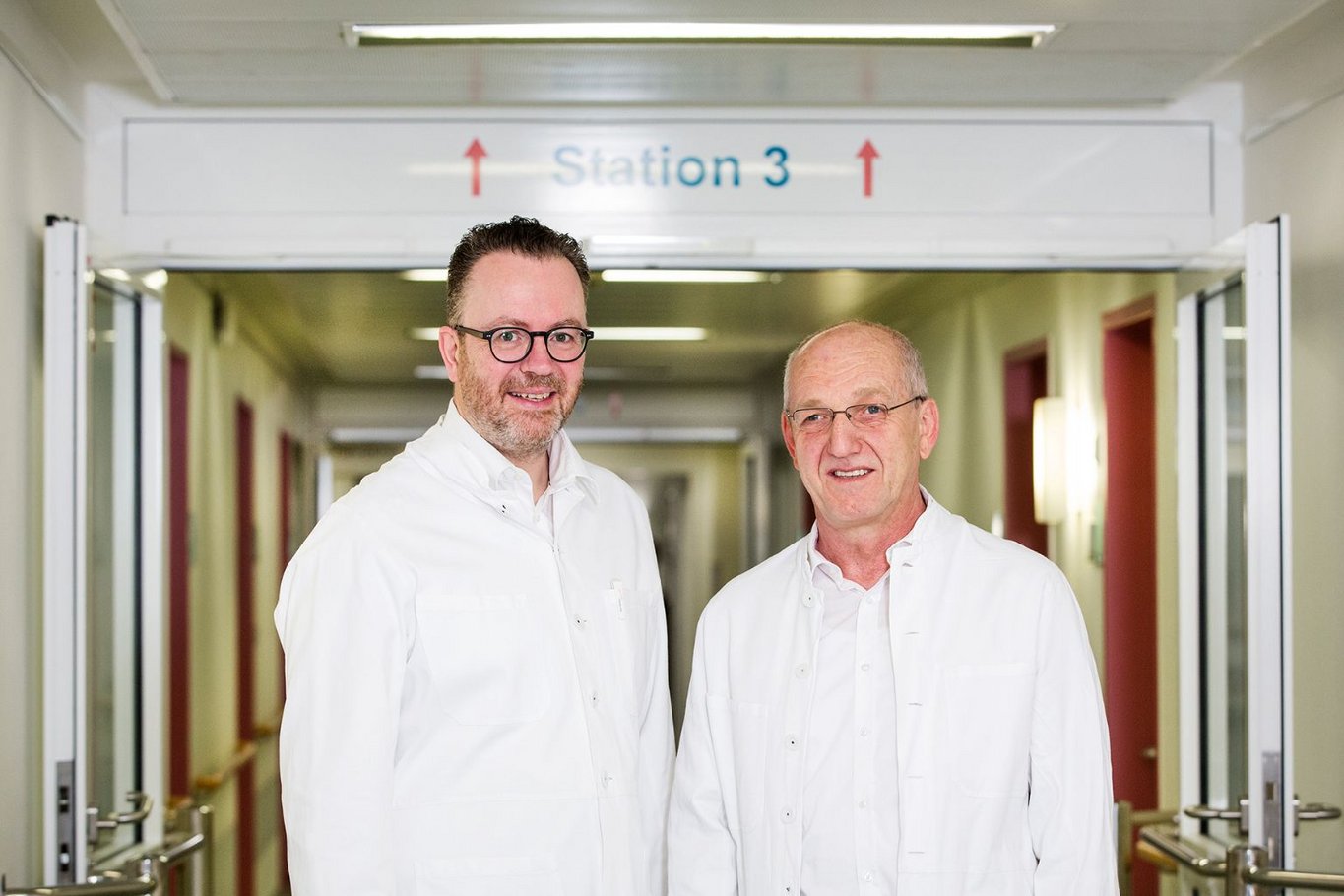Dr. Claus Brunken und Dr. Walter Wagner stehen in weißen Arztkitteln auf dem Flur vor Station 3 im Krankenhaus Reinbek St. Adolf-Stift.