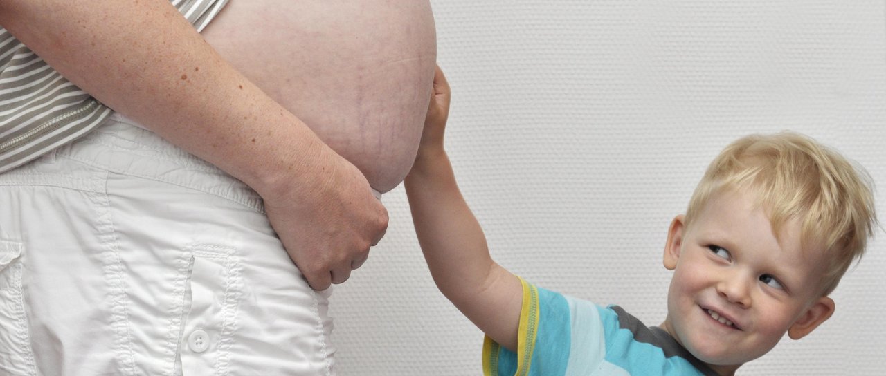 Ein kleiner Jung hält den schwangeren Bauch seiner Mama