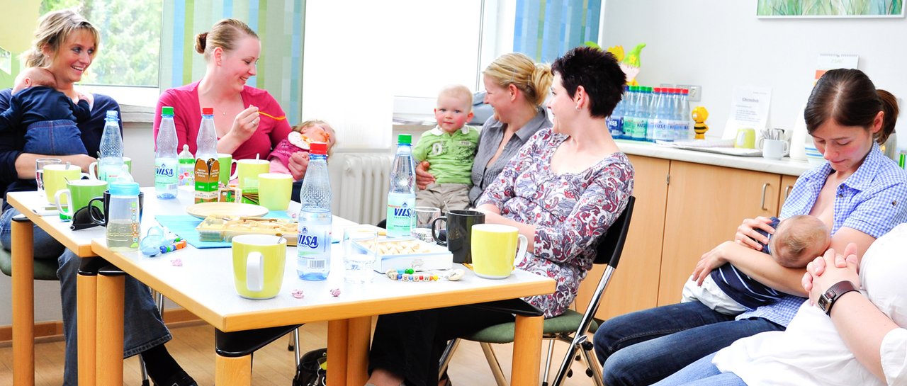 Mütter sitzen mit ihren Babys am Esstisch und unterhalten sich