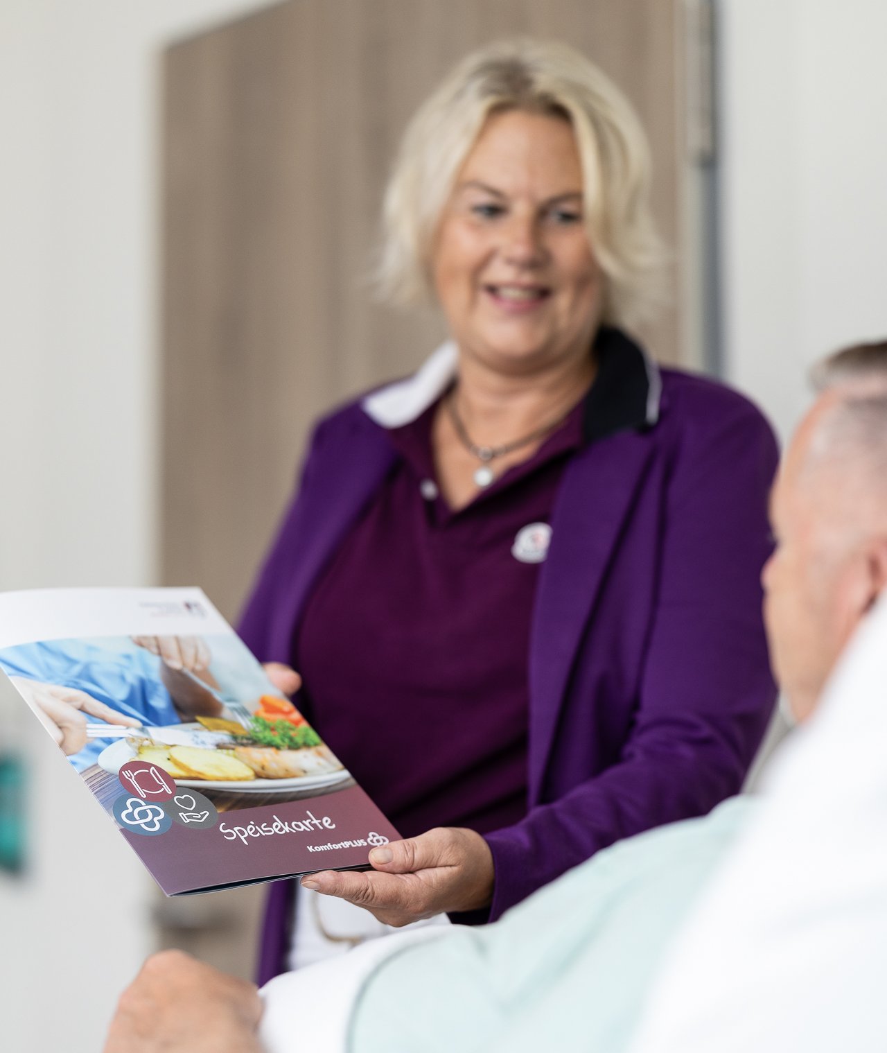 Eine Dame übergibt einem Patienten im Krankenhausbett die Speisekarte