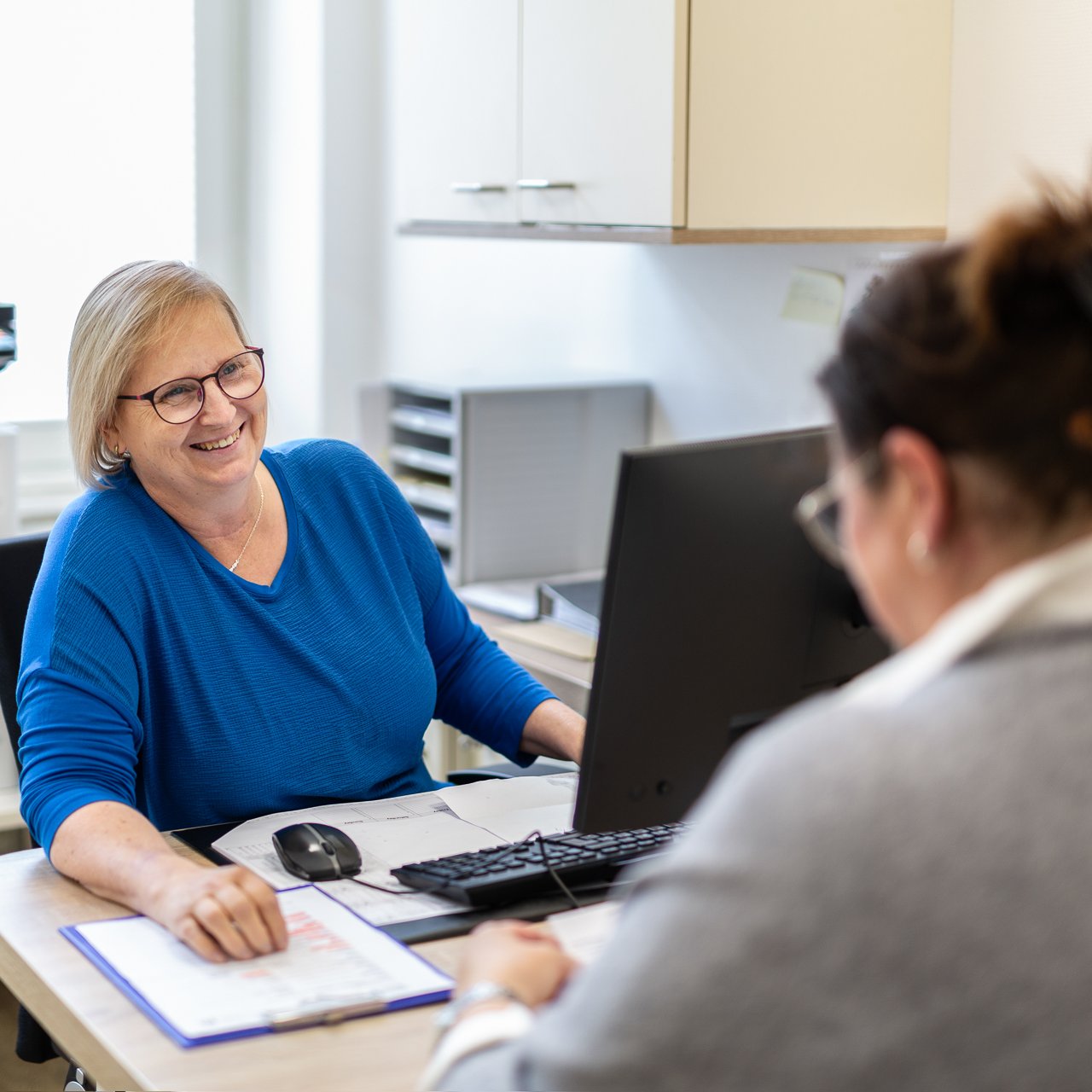 Eine Patientin beim Gespräch mit einer Sekretärin im Büro