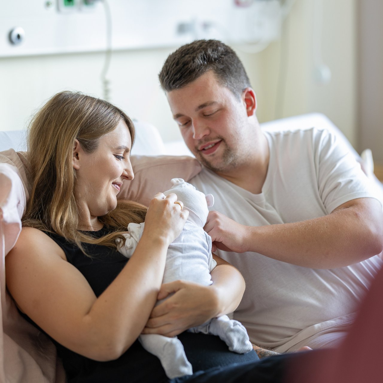 Zwei frisch-gebackene Eltern schauen liebevoll ihr Baby an
