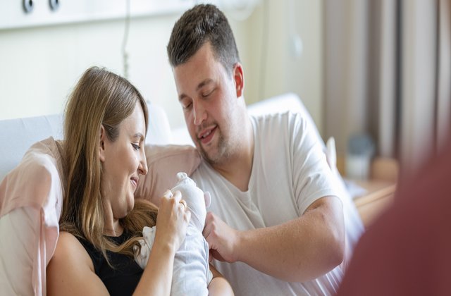 Zwei frisch-gebackene Eltern schauen liebevoll ihr Baby an