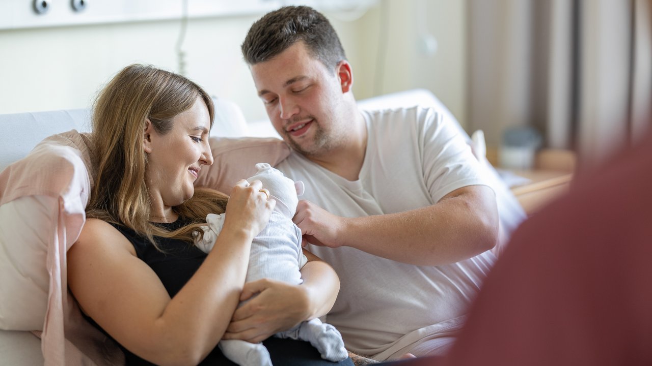 Zwei frisch-gebackene Eltern schauen liebevoll ihr Baby an
