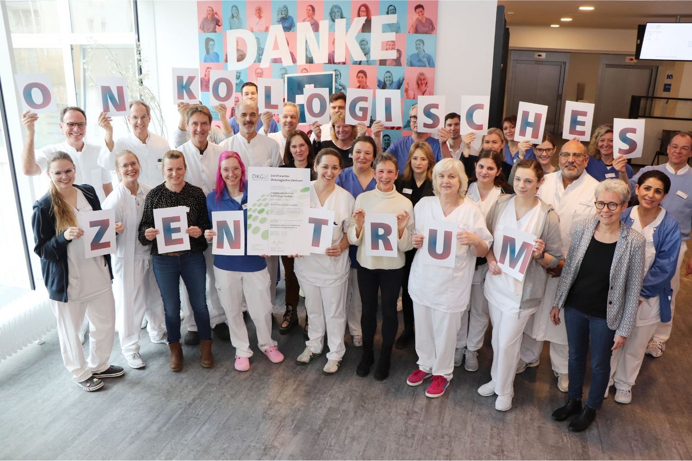 Große Gruppe von Mitarbeitenden des Krankenhauses Reinbek hält Buchstaben und ein Zertifikat und feiert die Anerkennung als Onkologisches Zentrum.