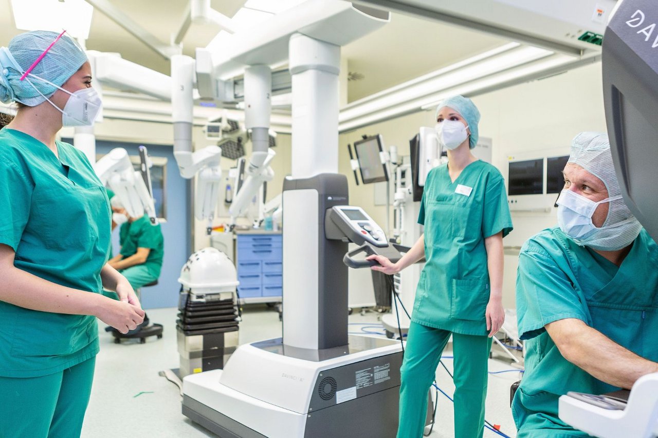 OP-Team in grüner Schutzkleidung steht in einem Operationssaal neben einem da Vinci-Operationssystem und bereitet einen Eingriff vor.