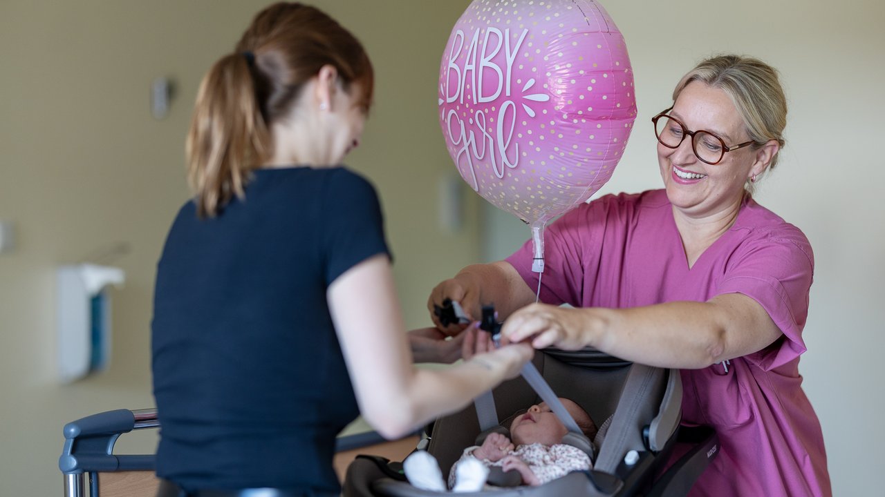 Eine Hebamme zeigt einer jungen Mutter, wie man ein Baby richtig im Auto sichert