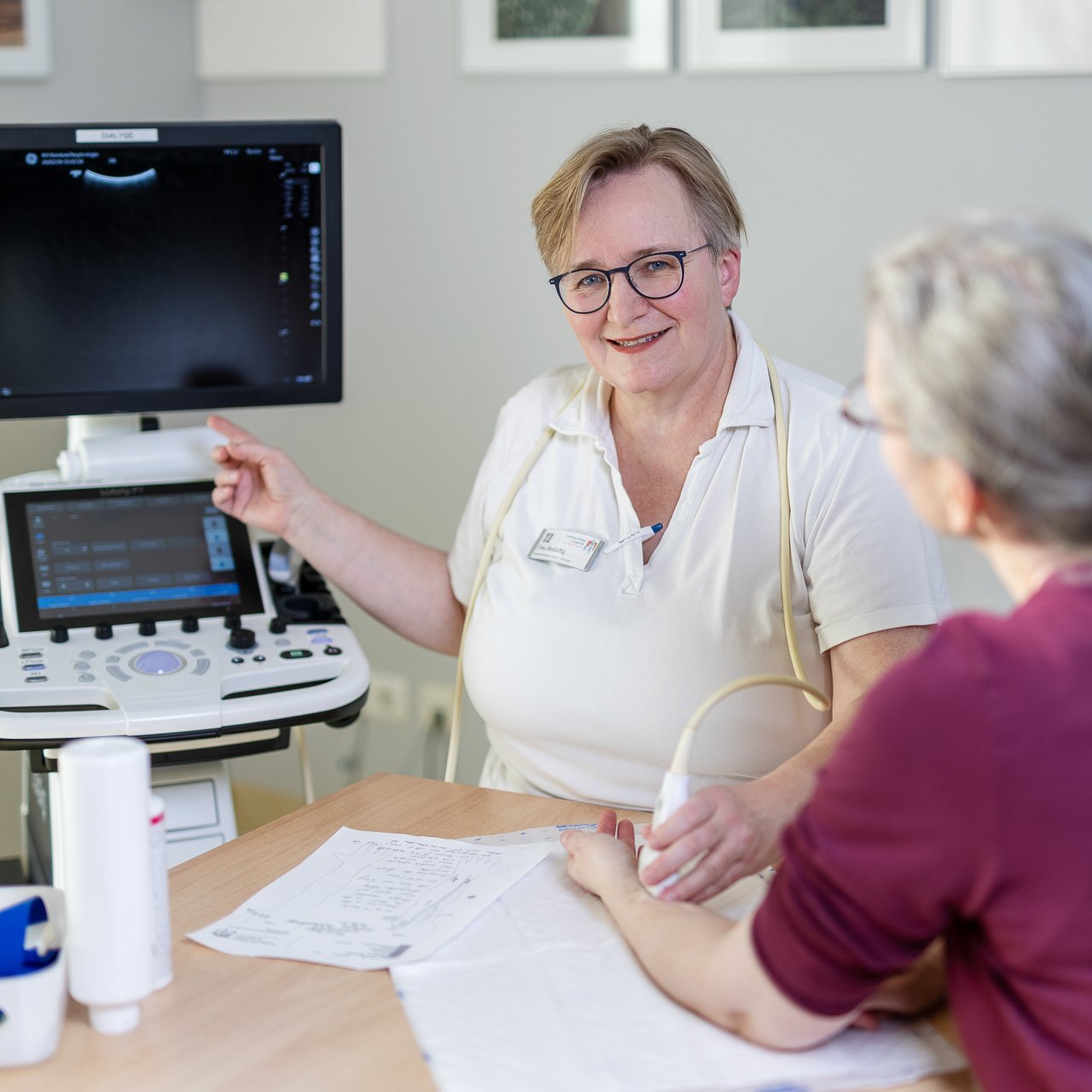 Eine Ärztin macht einen Ultraschal am Unterarm einer Patientin und lächelt