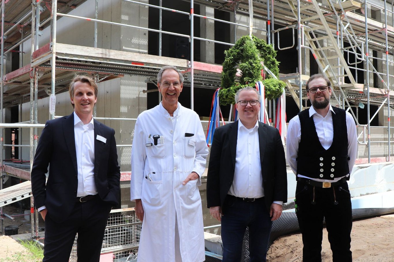Vier Männer stehen vor einem im Bau befindlichen Gebäude mit Gerüst beim Richtfest des Neubaus am Krankenhaus Reinbek St. Adolf-Stift.