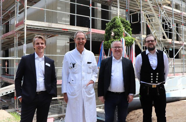 Vier Männer stehen vor einem im Bau befindlichen Gebäude mit Gerüst beim Richtfest des Neubaus am Krankenhaus Reinbek St. Adolf-Stift.