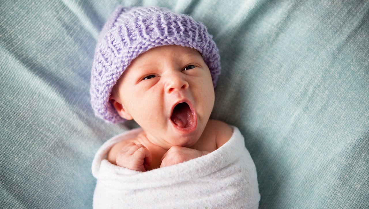 Neugeborenes Baby mit gestrickter Mütze gähnt.