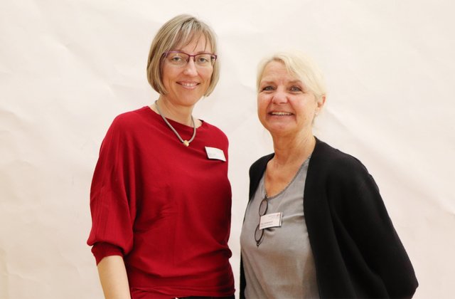 Zwei Frauen stehen nebeneinander vor hellem Hintergrund und lächeln in die Kamera, während sie die neue OTA-Ausbildungsmöglichkeit am St. Adolf-Stift repräsentieren.